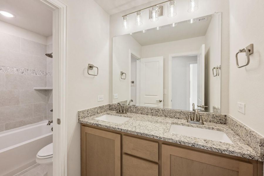 Bathroom with double sink vanity, granite countertop, large mirror, and tiled shower-tub combo Bathroom with double sink vanity, granite countertop, large mirror, and tiled shower-tub combo