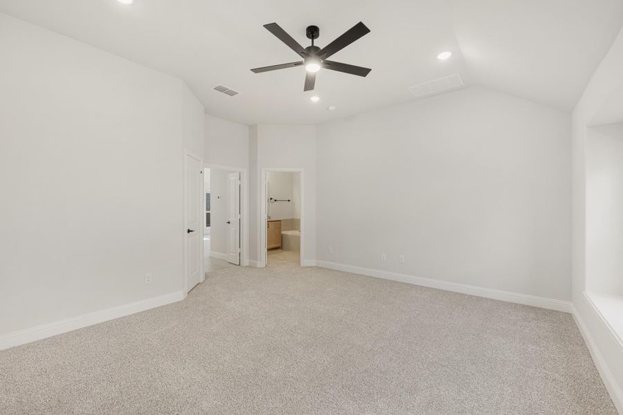 Empty bedroom with vaulted ceiling, black ceiling fan, carpet flooring, and open ensuite bathroom doorway.
