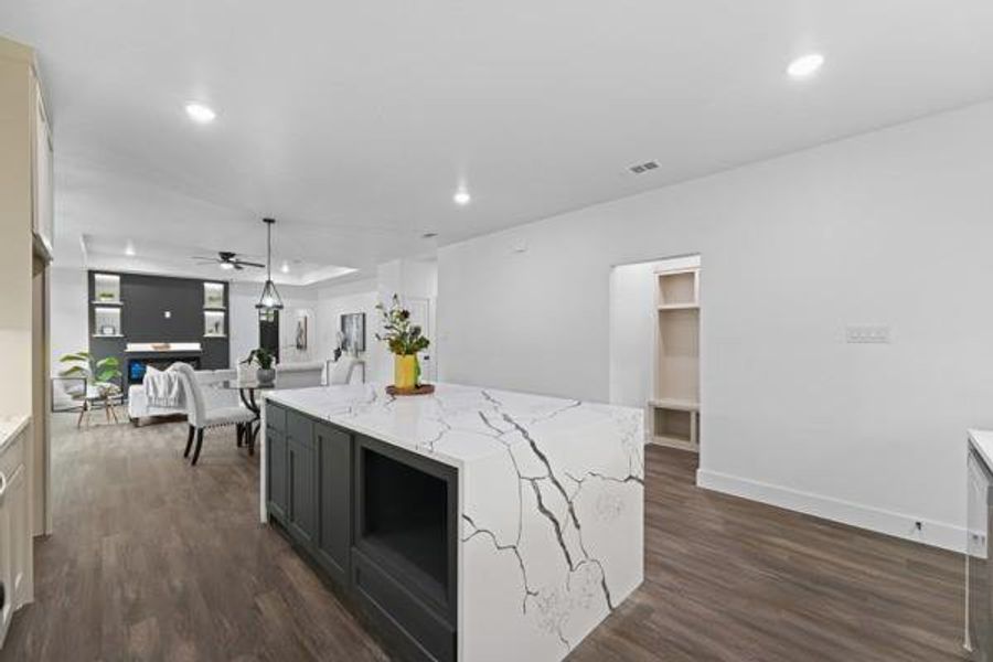 Kitchen island featuring a waterfall countertop with dark veining, integrated shelving, and dark base cabinetry Kitchen island featuring a waterfall countertop with dark veining, integrated shelving, and dark base cabinetry