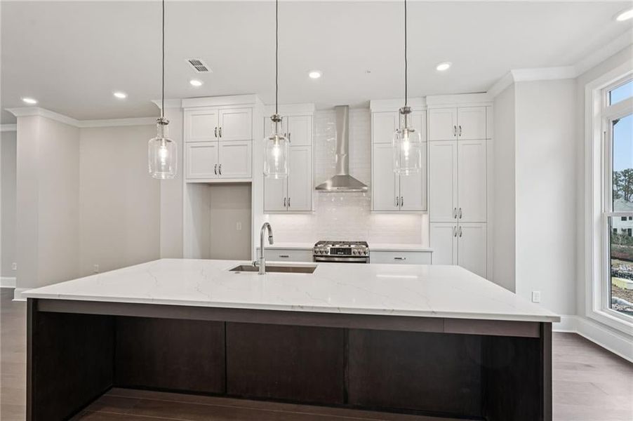 Two tone kitchen with crown molding, dark wood-type flooring, decorative light fixtures, stainless steel gas range, and light stone countertops