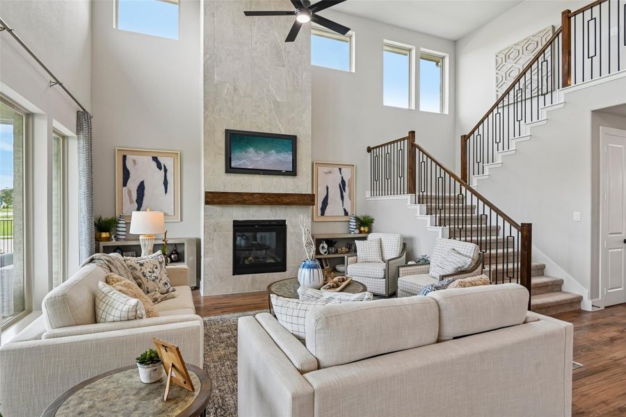Living room with two-story ceiling, tile fireplace, ceiling fan, and staircase with iron balusters Living room with two-story ceiling, tile fireplace, ceiling fan, and staircase with iron balusters