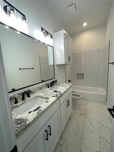 Bathroom featuring marble look tiles, double vanity, and shower / bath combination Bathroom featuring marble look tiles, double vanity, and shower / bath combination