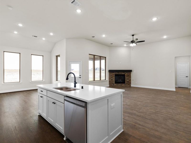 Kitchen with open floor plan, white cabinets, dishwasher, a fireplace, and an island with sink