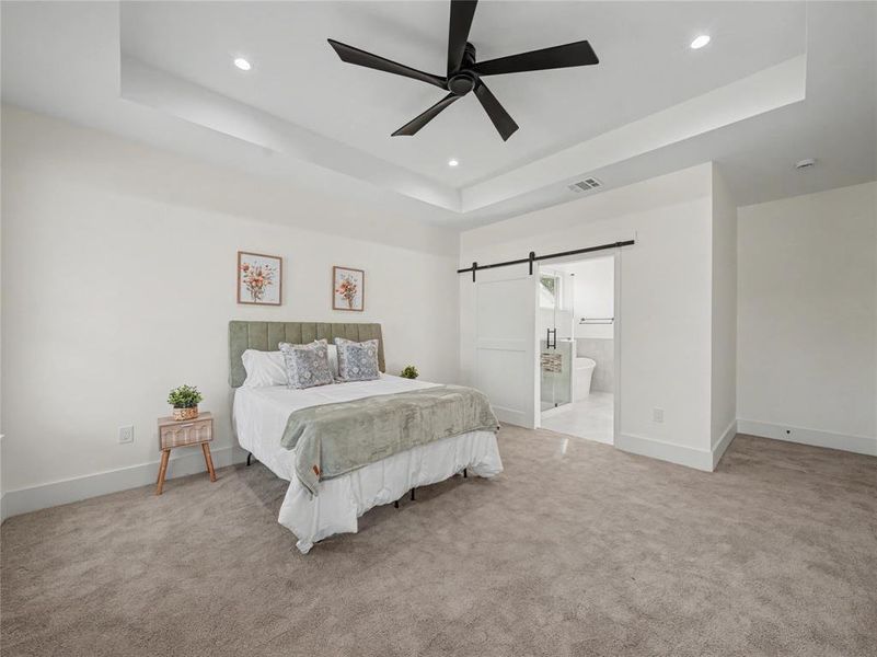 Bedroom featuring a barn door, a tray ceiling, light colored carpet, a ceiling fan, and recessed lighting