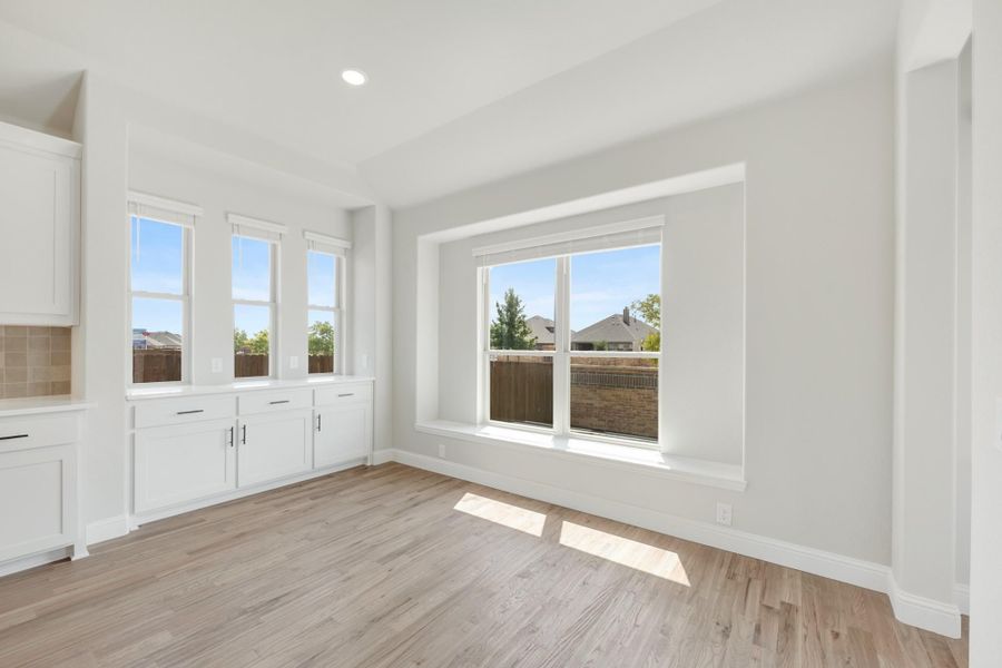 Bright dining area with light wood floors, white built-in cabinets, and large windows with backyard view Bright dining area with light wood floors, white built-in cabinets, and large windows with backyard view