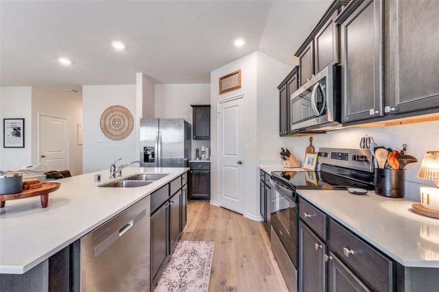 Kitchen with stainless steel appliances, light wood finished floors, light stone countertops, recessed lighting, and a center island with sink