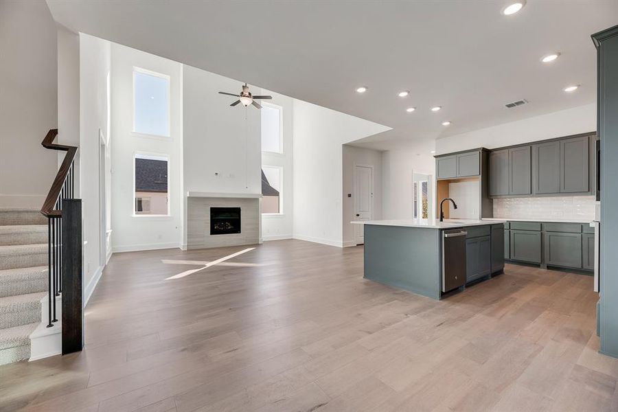 Kitchen featuring a center island with sink, open floor plan, a fireplace, tasteful backsplash, and light wood-style flooring