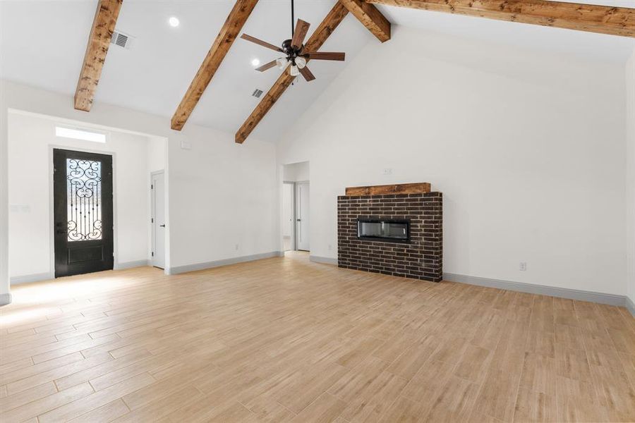 Unfurnished living room with high vaulted ceiling, ceiling fan, a brick fireplace, light wood-type flooring, and beamed ceiling