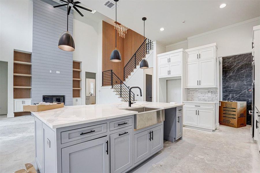 Kitchen with white cabinetry, sink, light stone counters, decorative light fixtures, and a center island with sink