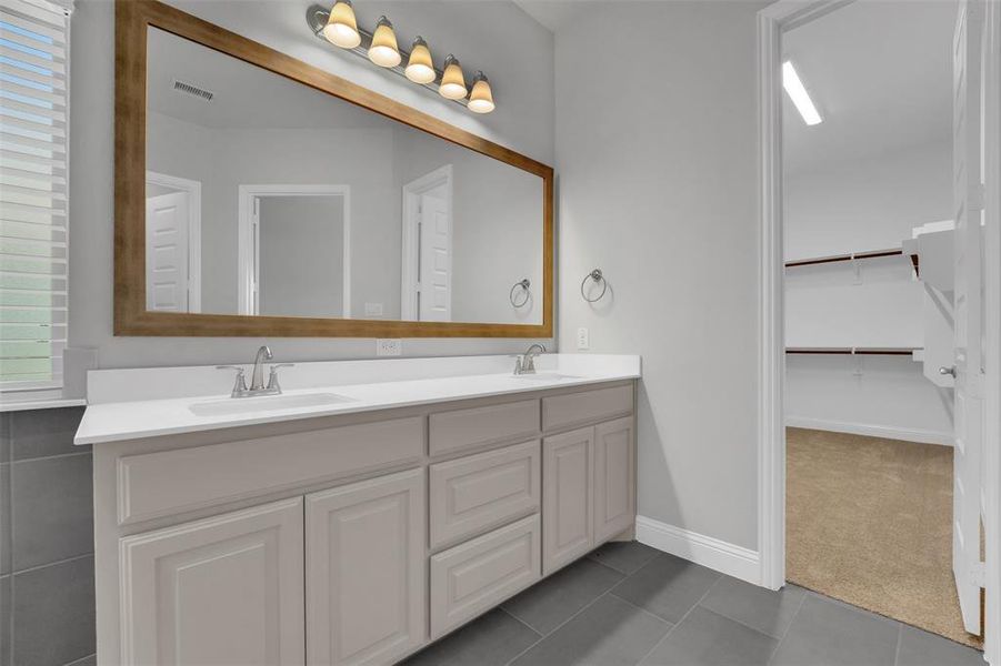 Full bathroom featuring double vanity, dark tile patterned flooring, a spacious closet, and dark colored carpet