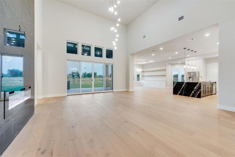 Unfurnished living room with light wood-style floors, a high ceiling, baseboards, and a sink Unfurnished living room with light wood-style floors, a high ceiling, baseboards, and a sink
