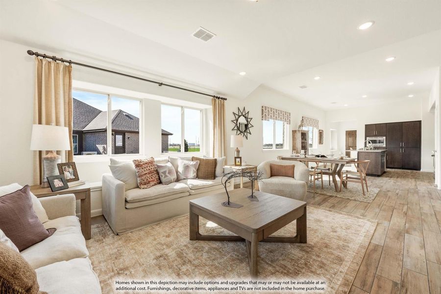Open-concept living room with vaulted ceiling, hardwood floors, and neutral furnishings leading to dining area and kitchen