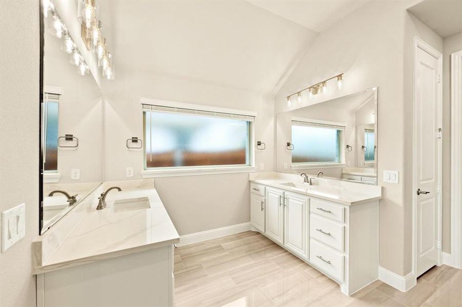 Bathroom featuring two vanities, vaulted ceiling, wood tiled floors, and plenty of natural light