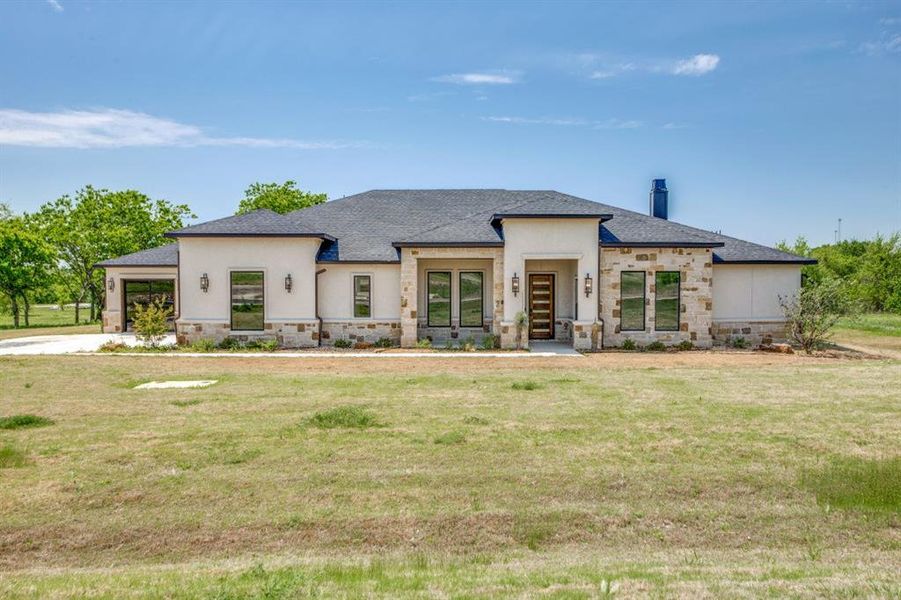 Prairie-style home featuring an attached garage, roof with shingles, stone siding, and a front lawn
