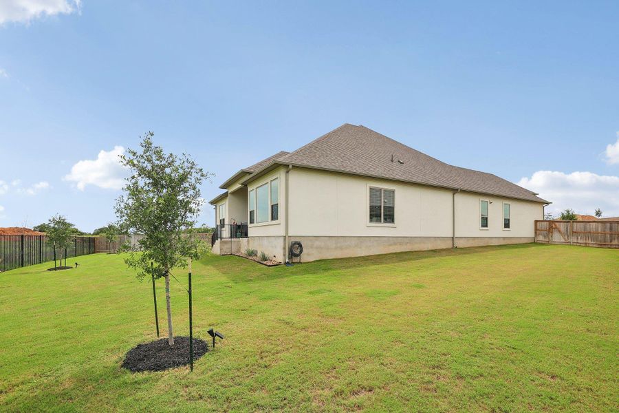 Expansive rear yard featuring a manicured lawn, established trees, and perimeter fencing