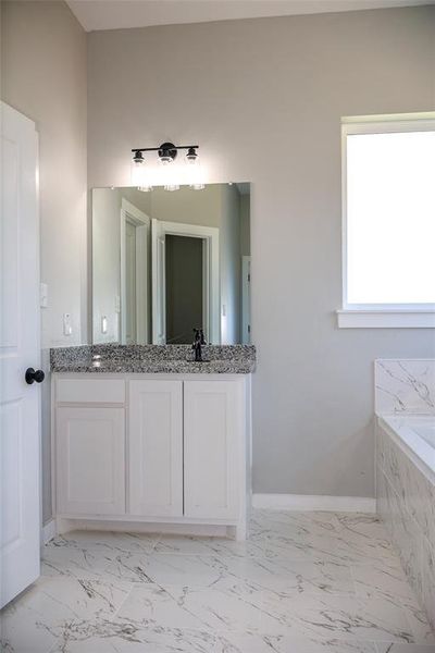 Bathroom featuring marble finish flooring, double vanity, and a tub with marble appearance