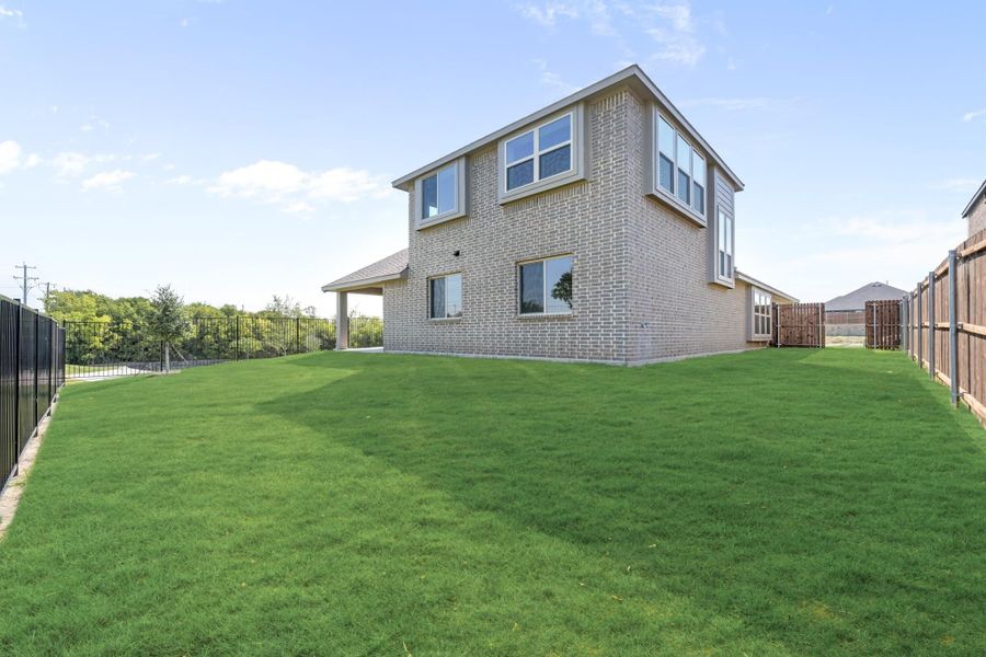 Two-story brick home with large grassy backyard and wood and metal fencing