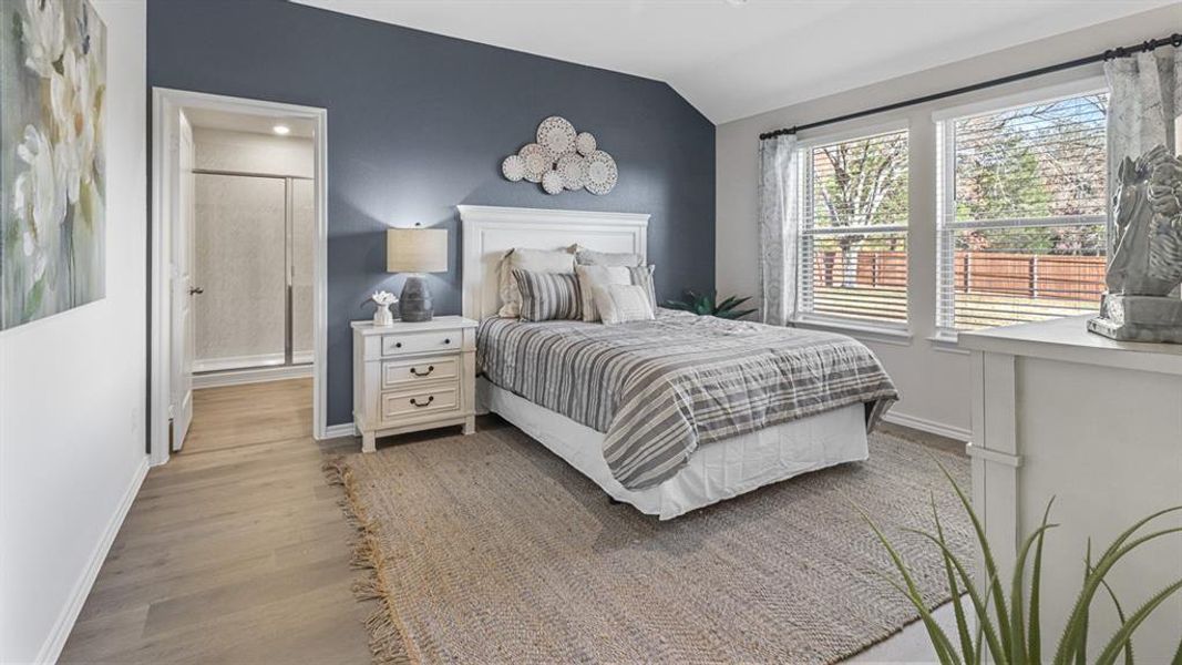 Bedroom with vaulted ceiling, wood finished floors, and ensuite bath