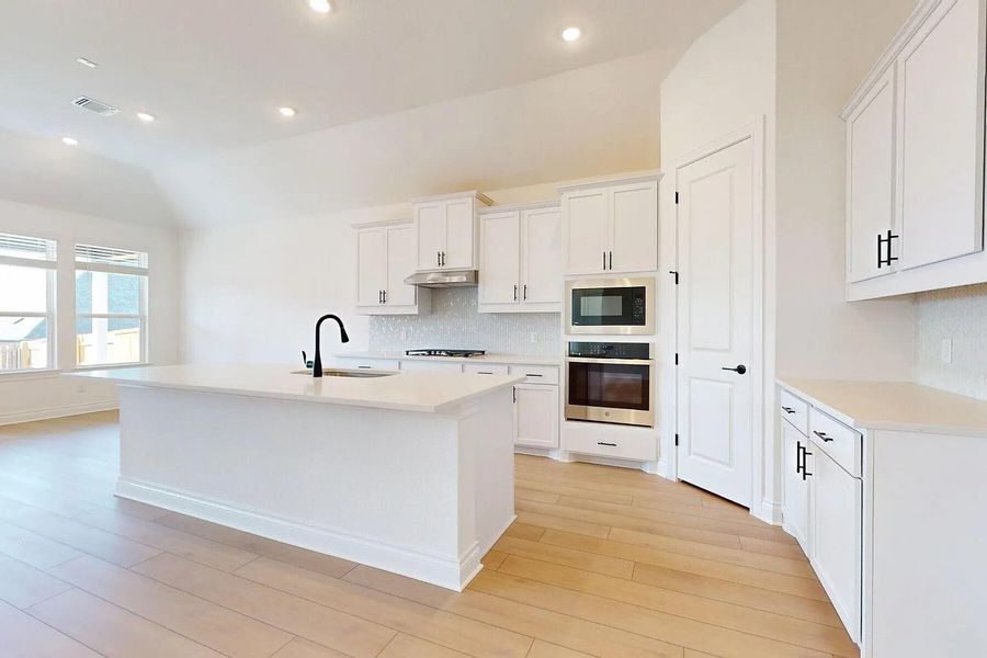 The kitchen features white cabinetry, stainless steel appliances, a white tile backsplash, and a large central island with a sink