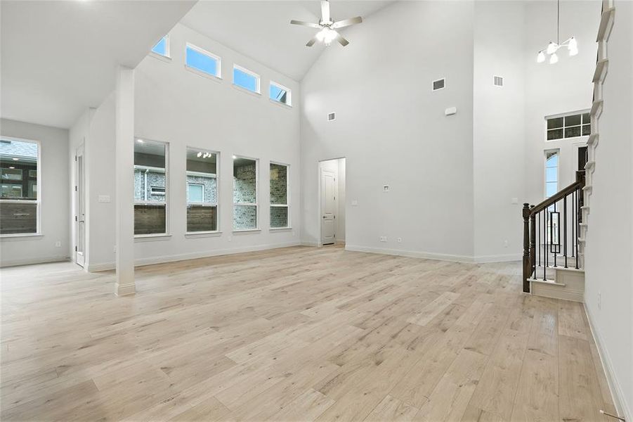 Unfurnished living room featuring light wood-style floors, a ceiling fan, healthy amount of natural light, stairs, and high vaulted ceiling
