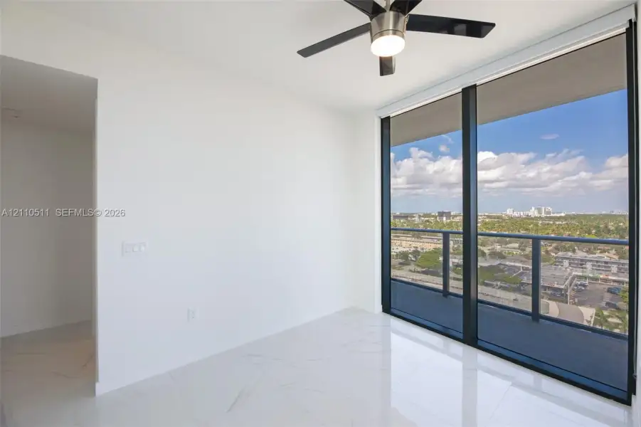 Second bedroom, floor-to-ceiling windows, high-gloss stone-finish flooring, private balcony with metal railing, and integrated ceiling fan with lighting