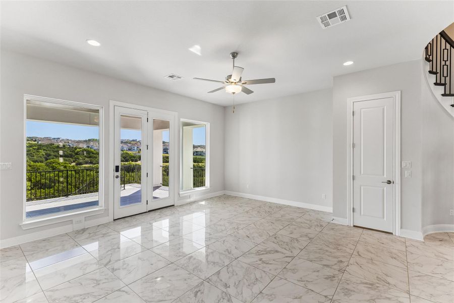 A luminous living space features gleaming tile flooring and a balcony with verdant outdoor views.