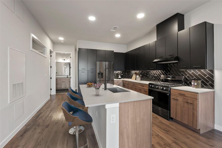 Kitchen with stainless steel appliances, under cabinet range hood, a sink, a breakfast bar, and backsplash