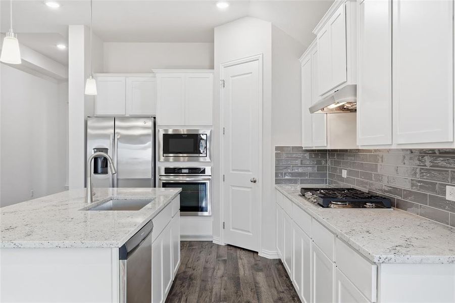 Modern kitchen featuring an island with a stainless steel sink, white shaker cabinetry, light granite countertops, stainless steel appliances, and wood-finish flooring