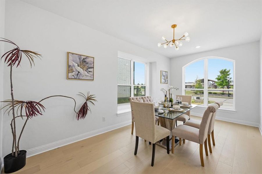 Dining area with light wood-finish flooring, an arched window, and a modern gold-tone chandelier