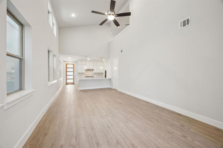 Unfurnished living room with ceiling fan, a towering ceiling, and light wood-type flooring