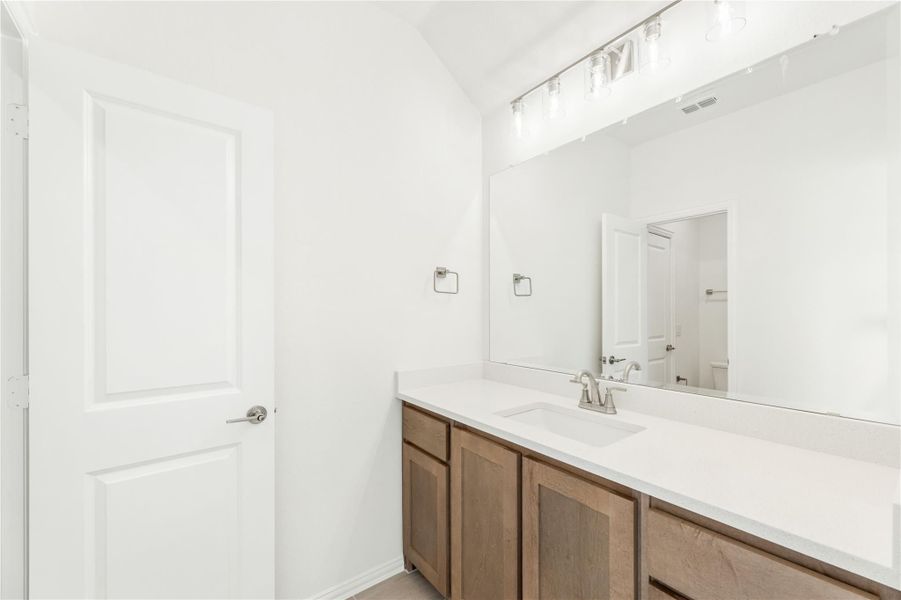 Bathroom vanity with wood cabinets, white countertop, single sink, and large mirror with overhead lighting