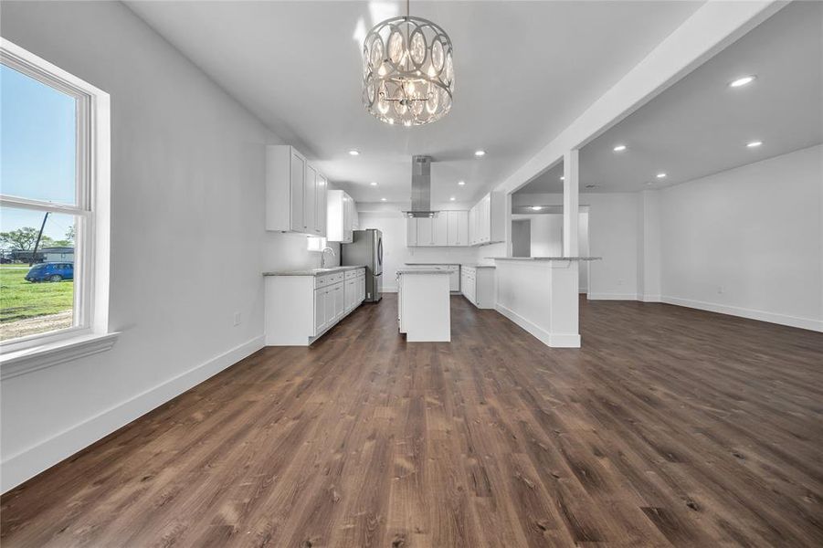 Kitchen featuring a notable chandelier, baseboards, open floor plan, dark wood-style floors, and freestanding refrigerator