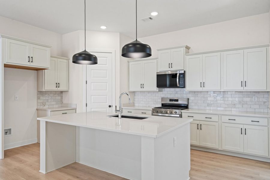 Kitchen with stainless steel appliances, a center island with sink, light wood finished floors, light stone counters, and white cabinets