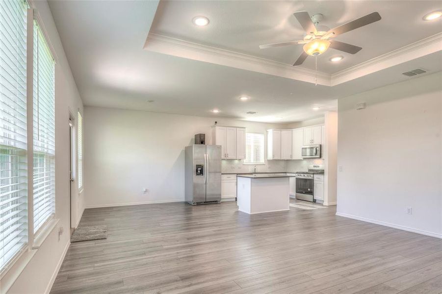 Living room with a tray ceiling, recessed lighting, luxury vinyl floor, a ceiling fan, and crown molding Living room with a tray ceiling, recessed lighting, luxury vinyl floor, a ceiling fan, and crown molding