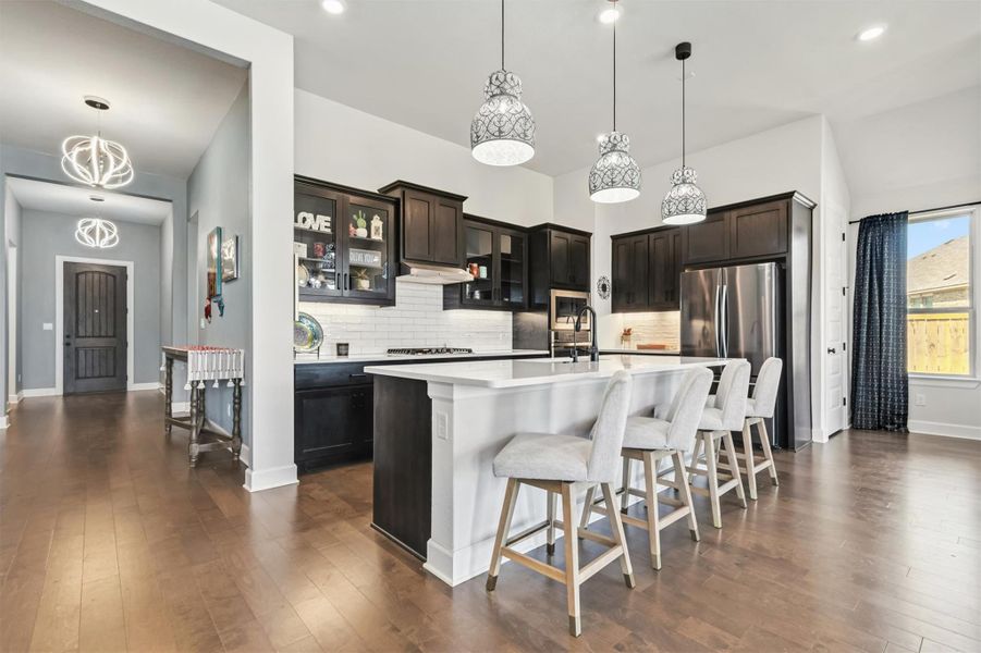Kitchen featuring glass insert cabinets, a kitchen breakfast bar, decorative light fixtures, tasteful backsplash, and a center island with sink Kitchen featuring glass insert cabinets, a kitchen breakfast bar, decorative light fixtures, tasteful backsplash, and a center island with sink
