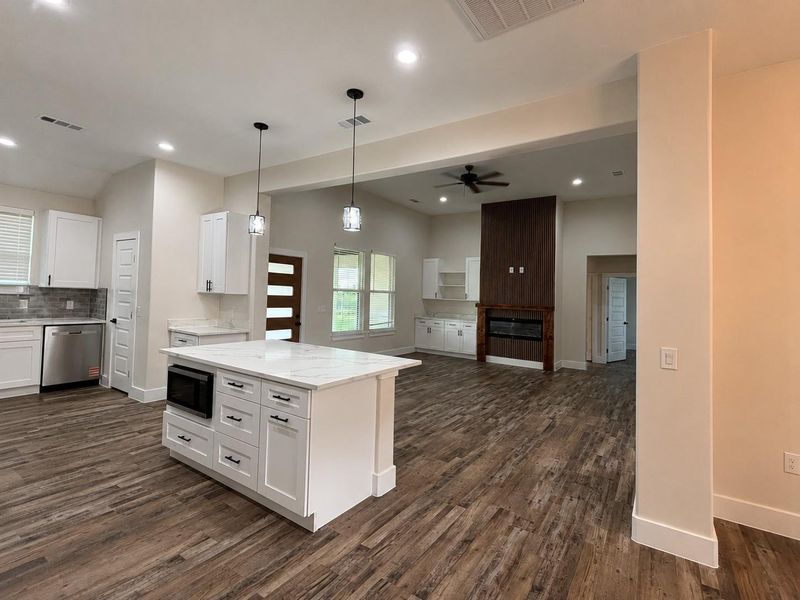 A contemporary open-concept space features a central kitchen island and a fireplace with a decorative wood panel.