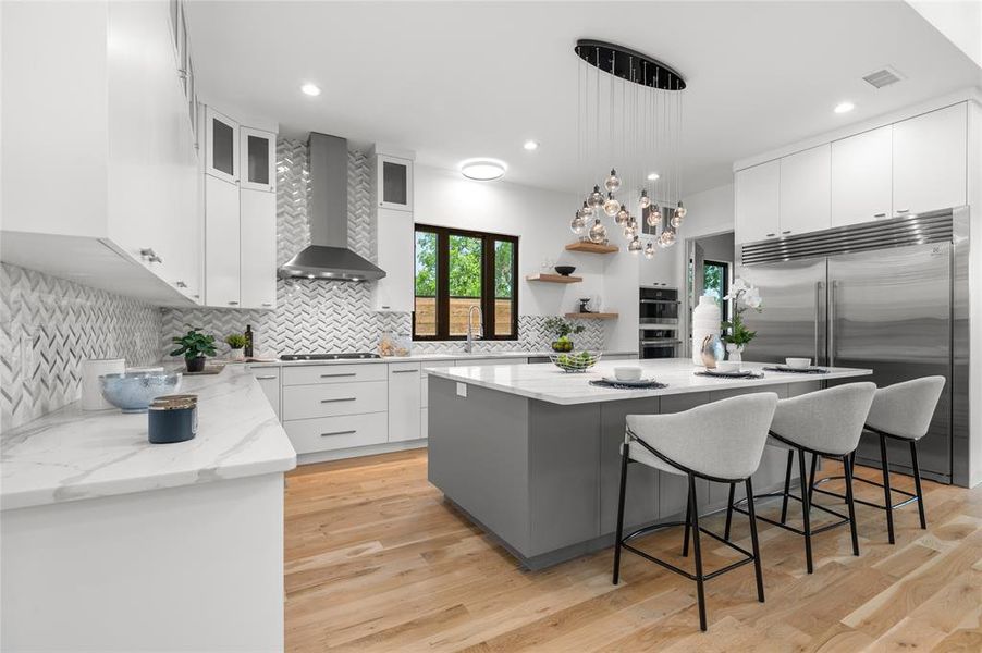 Kitchen with appliances with stainless steel finishes, light hardwood / wood-style floors, white cabinets, a center island, and wall chimney range hood