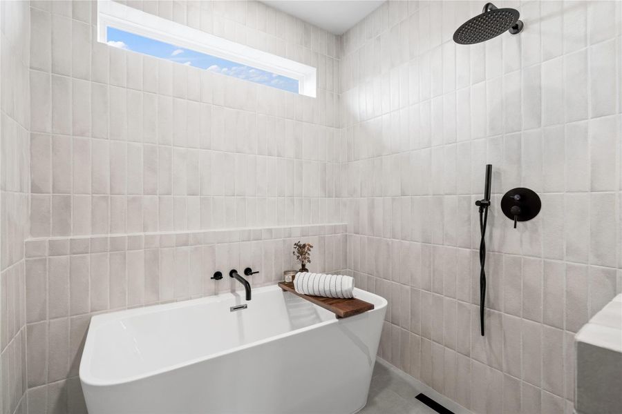 Tucked beneath a picture window and surrounded by floor-to-ceiling tile, this freestanding tub offers a luxurious escape within the walk-in wet room. Matte black fixtures and spa-style detailing create a serene, high-design space where you can unwind in total tranquility. Tucked beneath a picture window and surrounded by floor-to-ceiling tile, this freestanding tub offers a luxurious escape within the walk-in wet room. Matte black fixtures and spa-style detailing create a serene, high-design space where you can unwind in total tranquility.