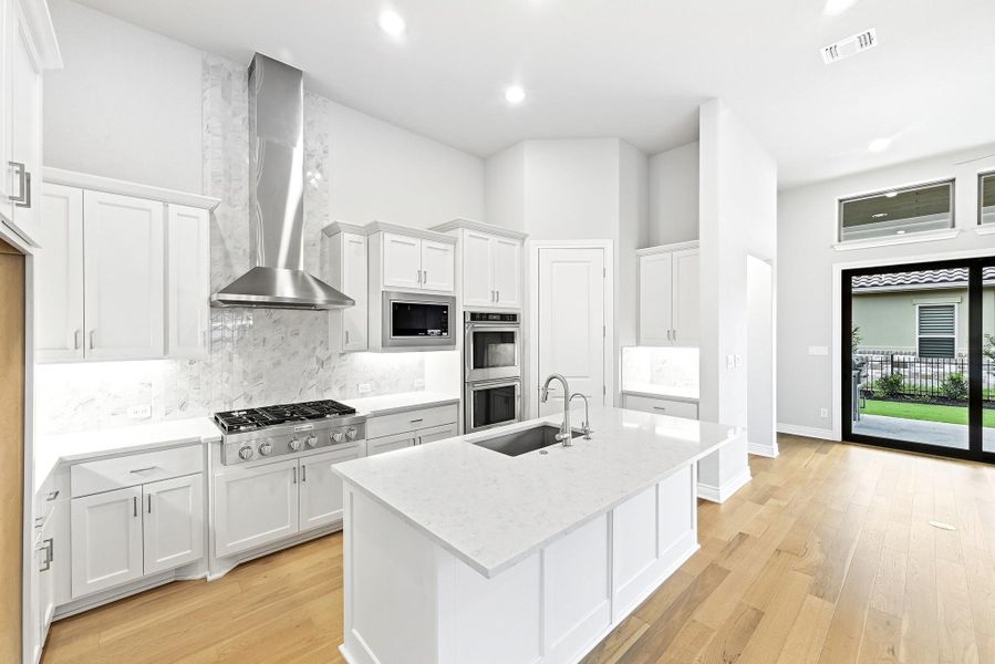 Modern kitchen featuring white shaker cabinetry, stainless steel appliances, a center island with sink and integrated dishwasher, a gas range with a large stainless steel hood, and wood-finish flooring