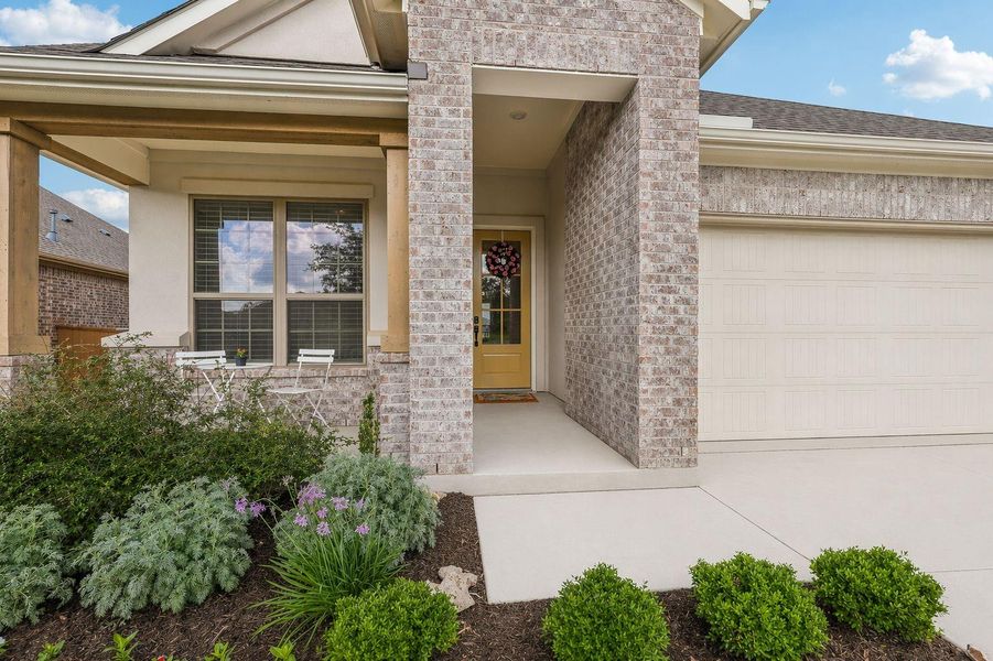 A welcoming brick exterior boasts lush landscaping and a cozy front porch with seating.