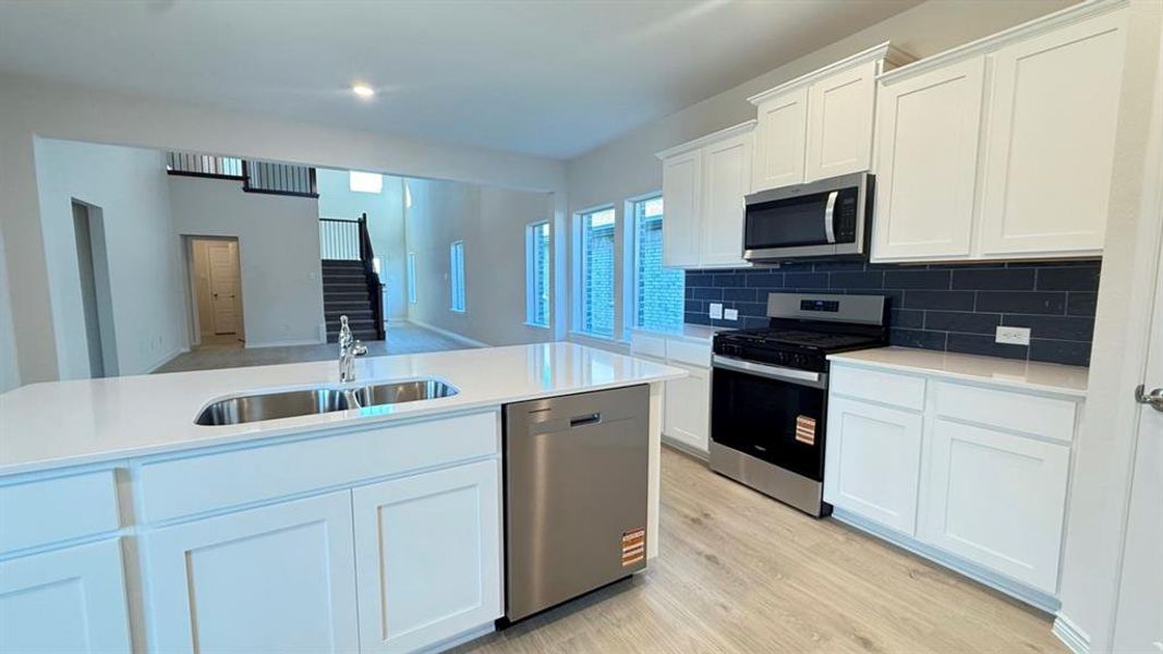 Kitchen with white cabinets, appliances with stainless steel finishes, light wood-style flooring, backsplash, and light stone countertops
