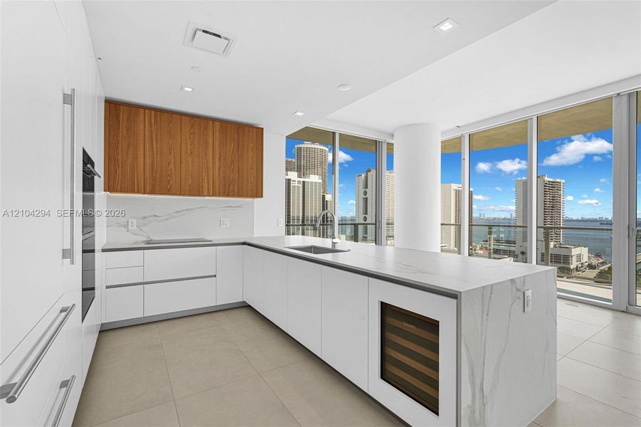 Sleek kitchen featuring white cabinetry, wood-finish upper cabinets, integrated stainless steel appliances, and a central island with a built-in wine refrigerator