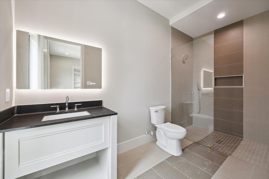 Designed with clean, contemporary style, this en-suite bathroom offers a quartz-topped vanity with an undermount sink and illuminated mirror. The large walk-in shower with a soap inset adds both function and elegance, creating a spa-like experience.