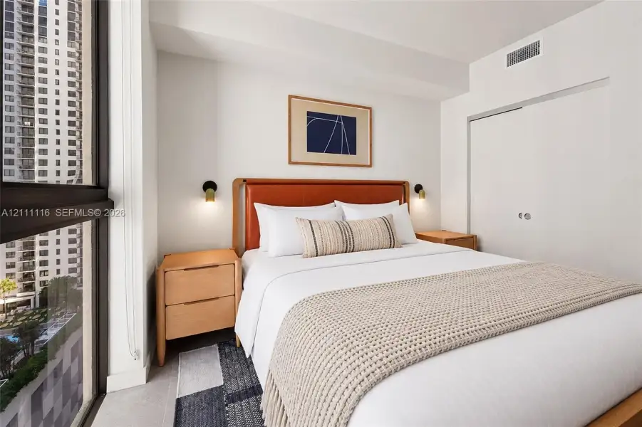 Floor-to-ceiling windows, dual wall-mounted light fixtures, and a built-in closet with sliding doors
