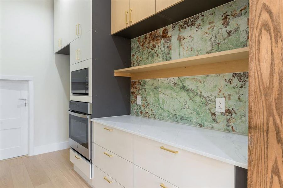 Kitchen featuring modern cabinets, light wood finished floors, oven, and light stone countertops