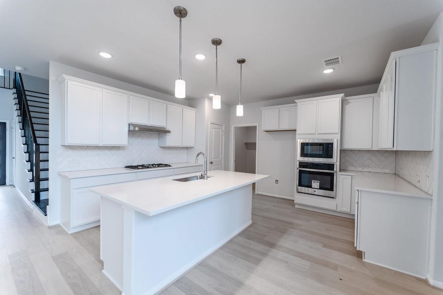 Kitchen with stainless steel appliances, light wood-style floors, white cabinetry, and light stone countertops