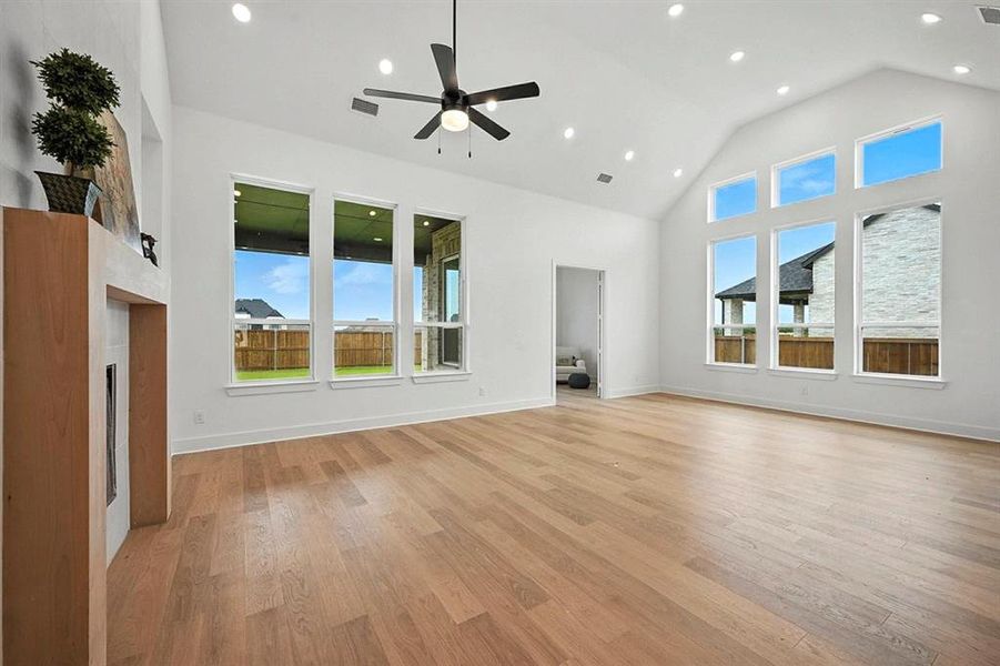 Unfurnished living room with high vaulted ceiling, a fireplace, healthy amount of natural light, light wood-style floors, and recessed lighting