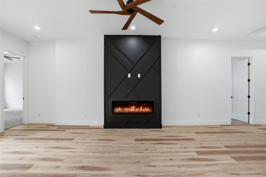Open-concept living space with wood-finish flooring, a contemporary fireplace feature wall, recessed lighting, and a modern ceiling fan