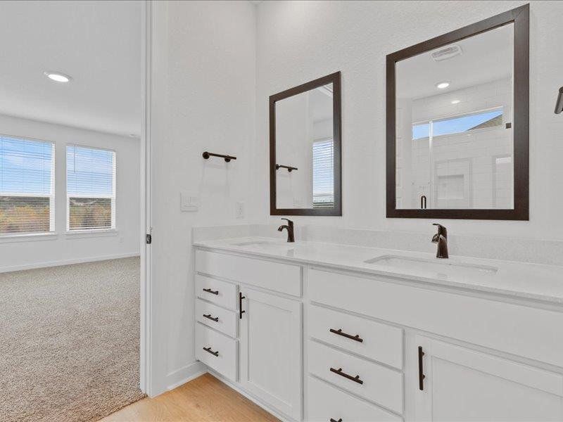 Bathroom featuring double vanity, light colored carpet, recessed lighting, and a shower