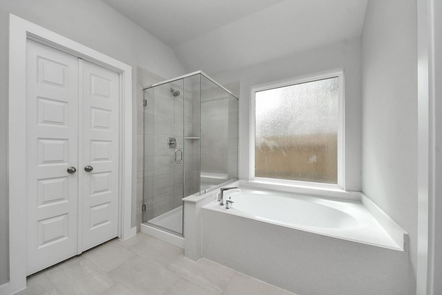 Escape to a spa-like oasis in this primary bathroom. Enjoy a walk-in shower with tile surround, a separate garden tub with custom detailing, and an elegant vanity featuring light countertops, modern hardware, and beautiful vanity lights. Experience luxury and relaxation in every detail. Sample photo of completed home with similar floor plan. Actual colors and selections may vary.